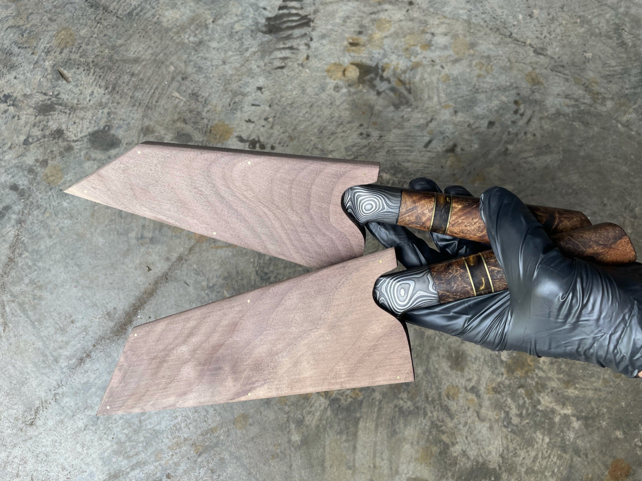 Two integral bolster knives with sheaths on concrete background held by gloved hand