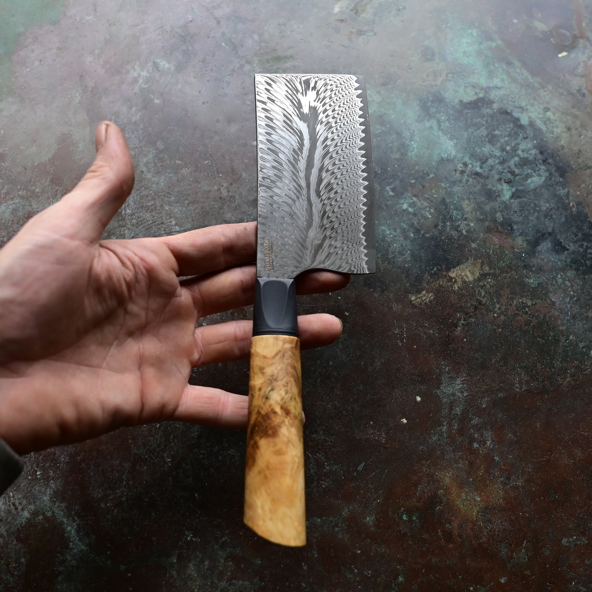 Unique mini cleaver on a concrete background, featuring a 4.5" long feather Damascus VG10 stainless blade, a sleek black anodized bolster, and a stabilized golden Buckeye burl wood handle with intricate patterns and color variations.
