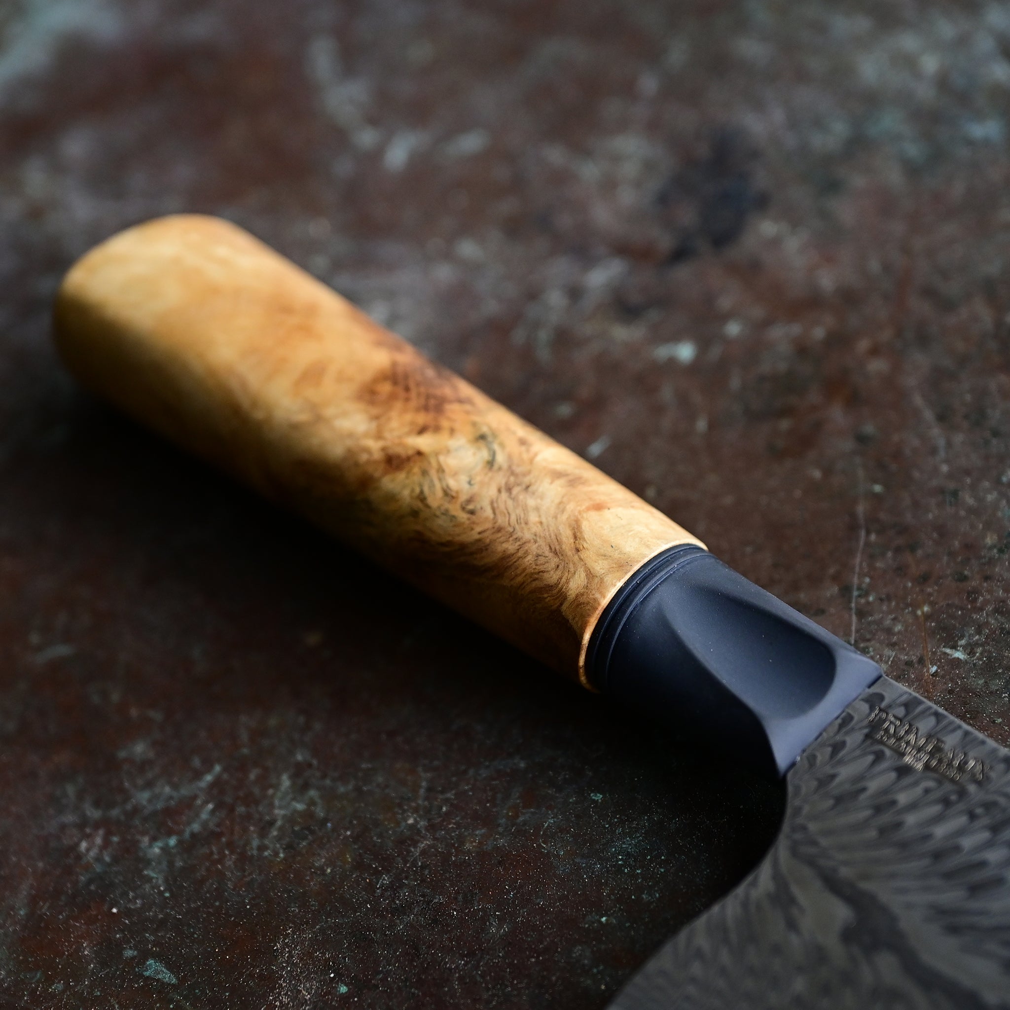 Unique mini cleaver on a concrete background, featuring a 4.5" long feather Damascus VG10 stainless blade, a sleek black anodized bolster, and a stabilized golden Buckeye burl wood handle with intricate patterns and color variations.