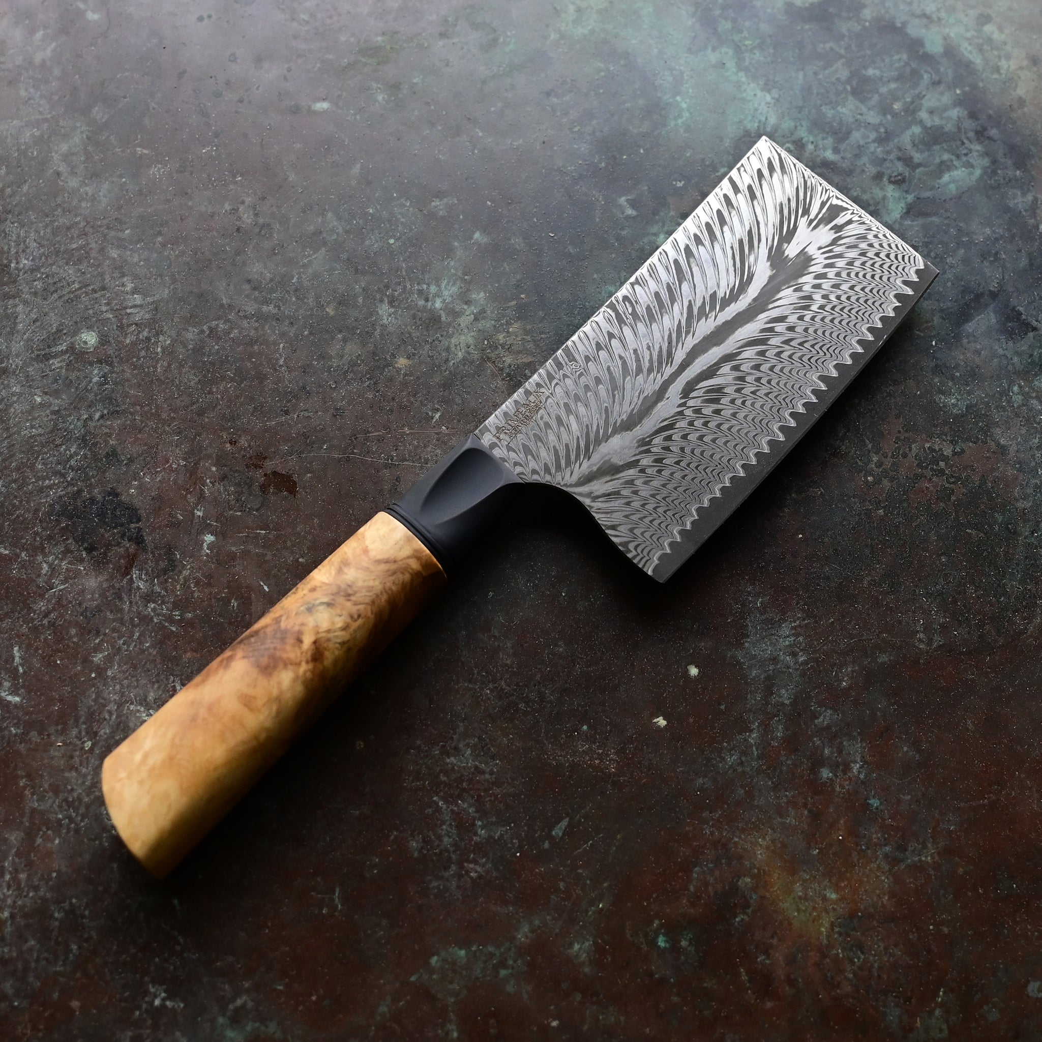 Unique mini cleaver on a concrete background, featuring a 4.5" long feather Damascus VG10 stainless blade, a sleek black anodized bolster, and a stabilized golden Buckeye burl wood handle with intricate patterns and color variations.