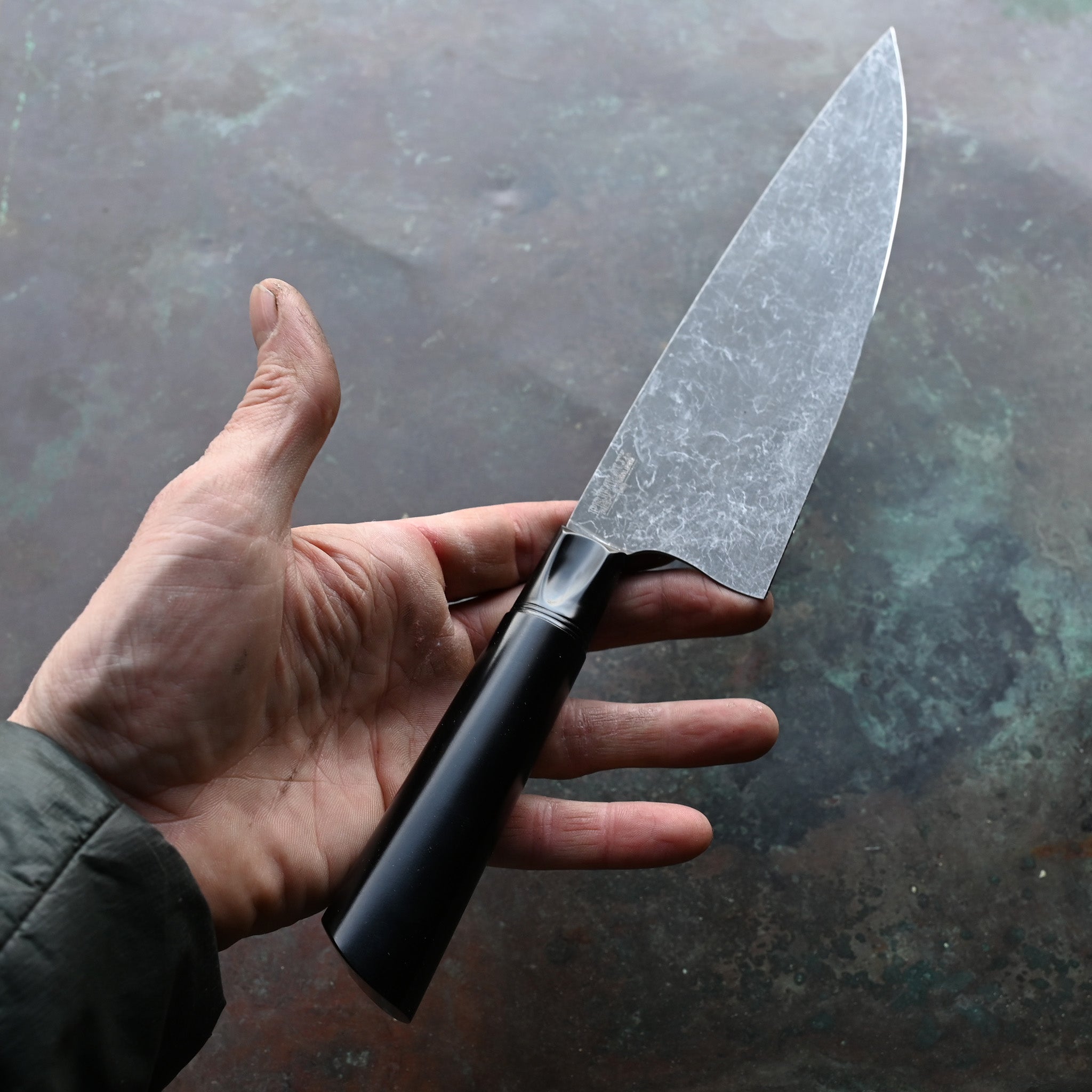 CHEF KNIFE ON CONCRETE BACKGROUND ANODIZED ALUMINUM BLACK HANDLE AND BOLSTER
