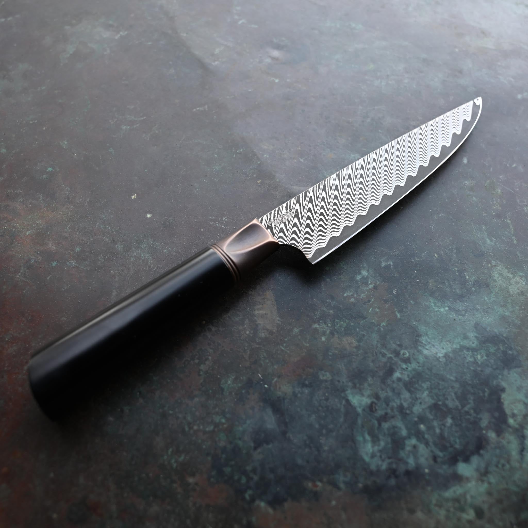 DAMASCUS STEEL PETTY KNIFE WITH ANTIQUE BOLSTER AND BLACK HANDLE ON CONCRETE BACKGROUND