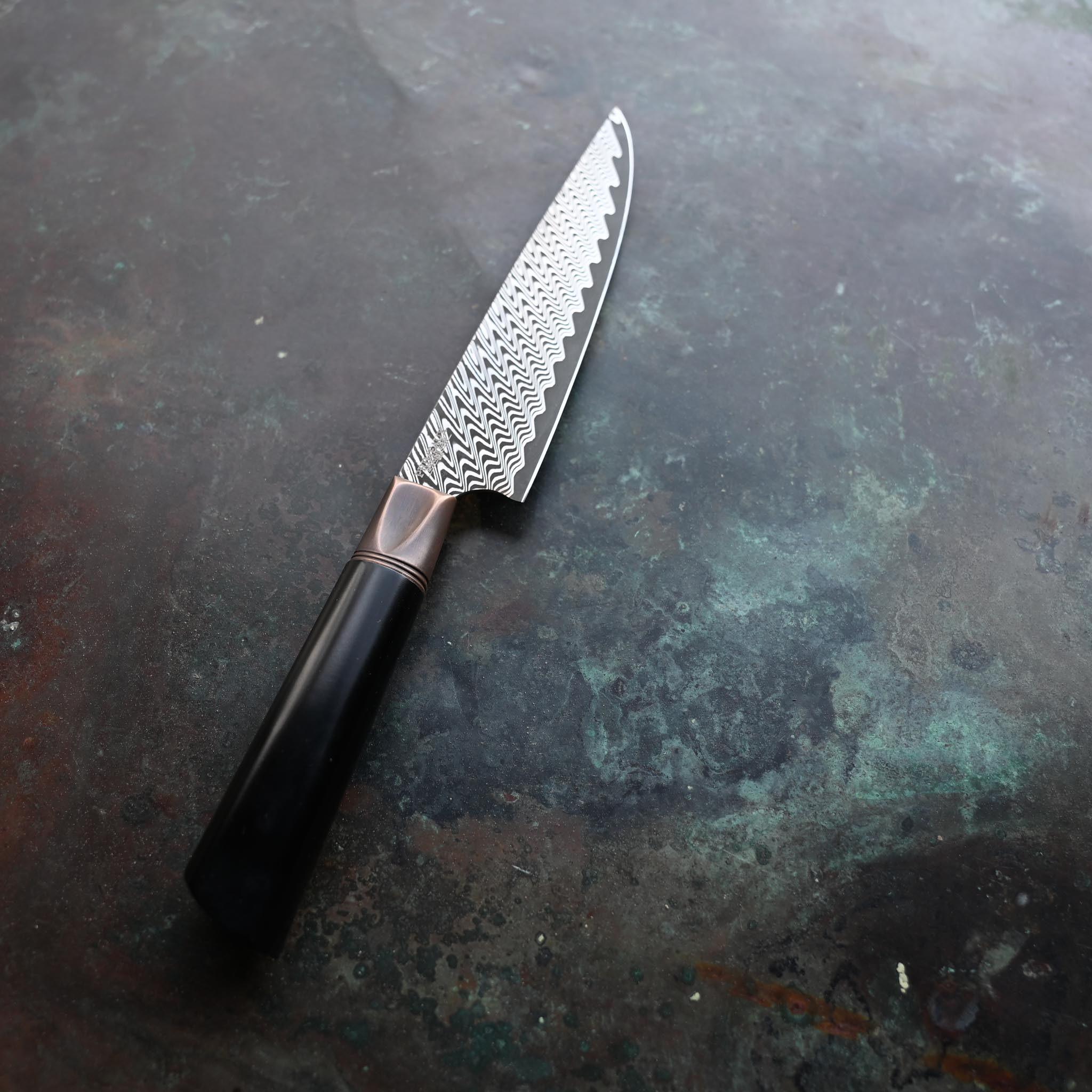DAMASCUS STEEL PETTY KNIFE WITH ANTIQUE BOLSTER AND BLACK HANDLE ON CONCRETE BACKGROUND