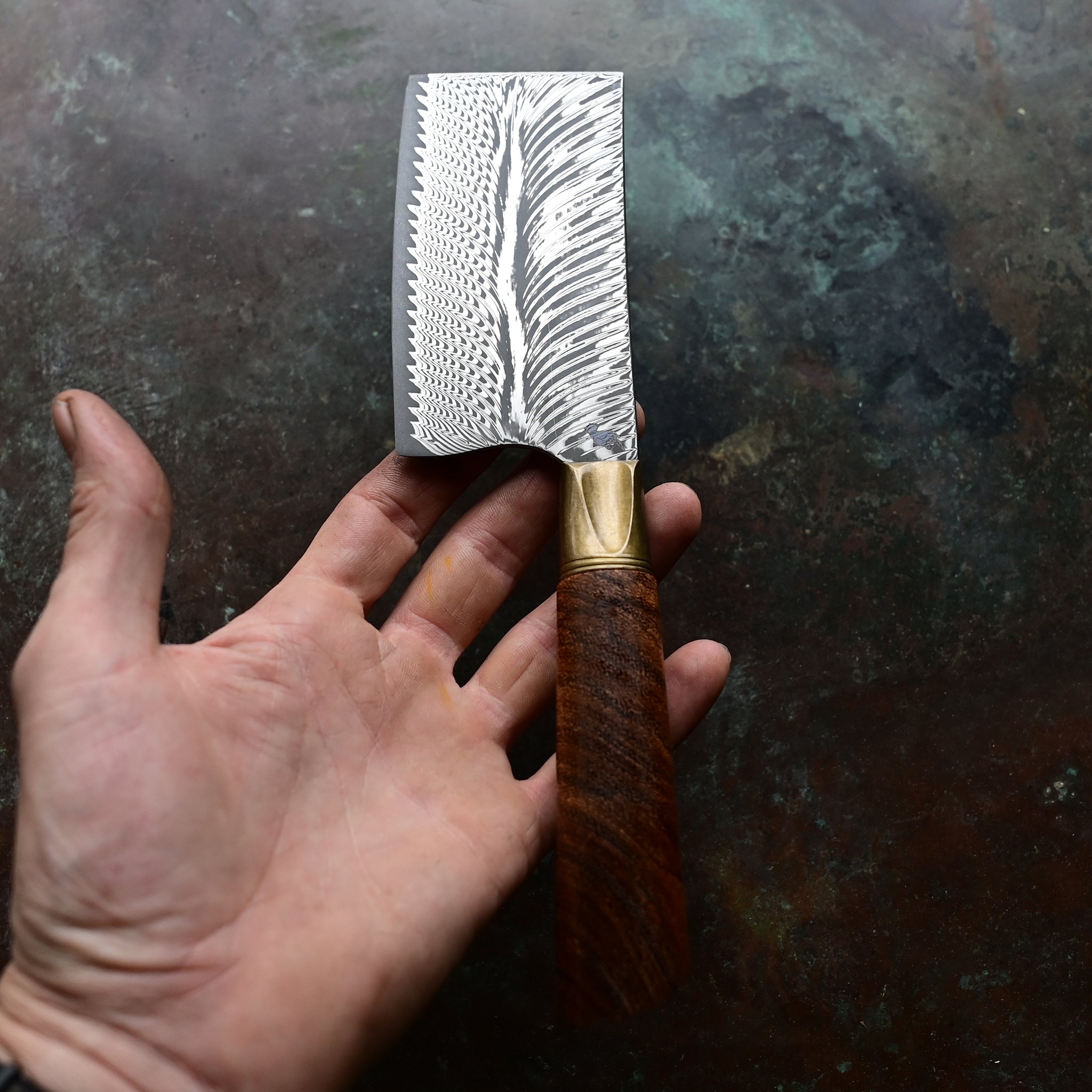 A mini cleaver with a bronze bolster, feather Damascus VG10 blade, and a Bocote wood handle, showcased on a concrete background