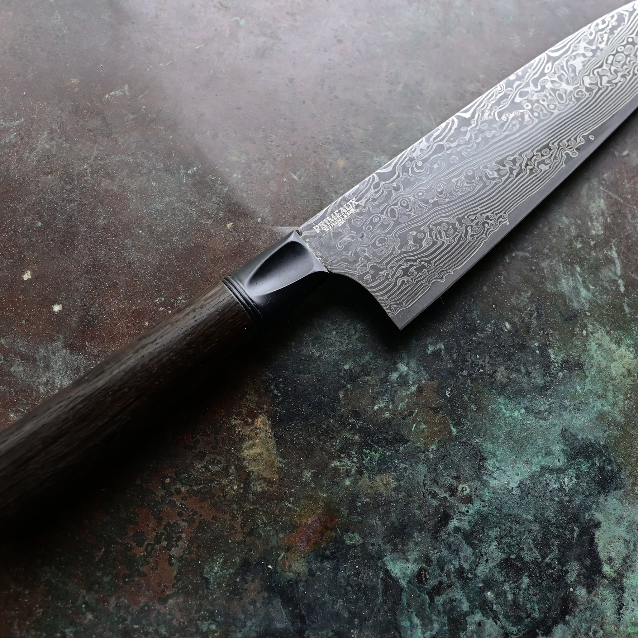 Hand-forged Santoku knife resting on a concrete background, featuring a deep black 7,000-year-old Irish bog oak handle, a contrasting silver anodized aluminum bolster, and a 7.5" VG10 stainless Damascus blade with intricate patterns.