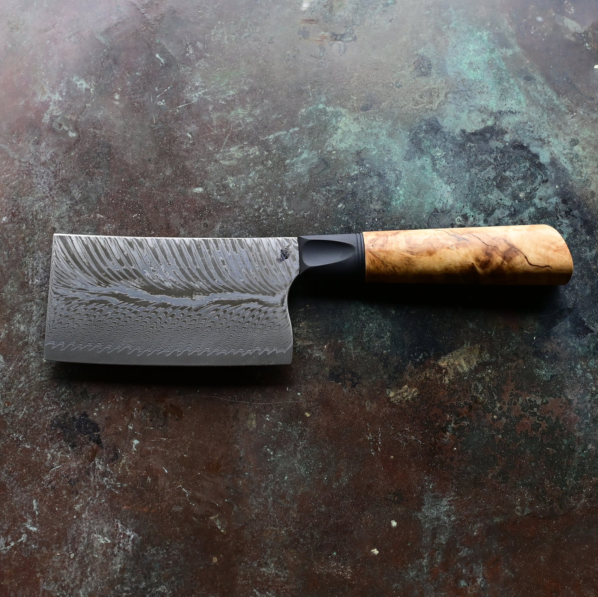 Unique mini cleaver on a concrete background, featuring a 4.5" long feather Damascus VG10 stainless blade, a sleek black anodized bolster, and a stabilized golden Buckeye burl wood handle with intricate patterns and color variations.