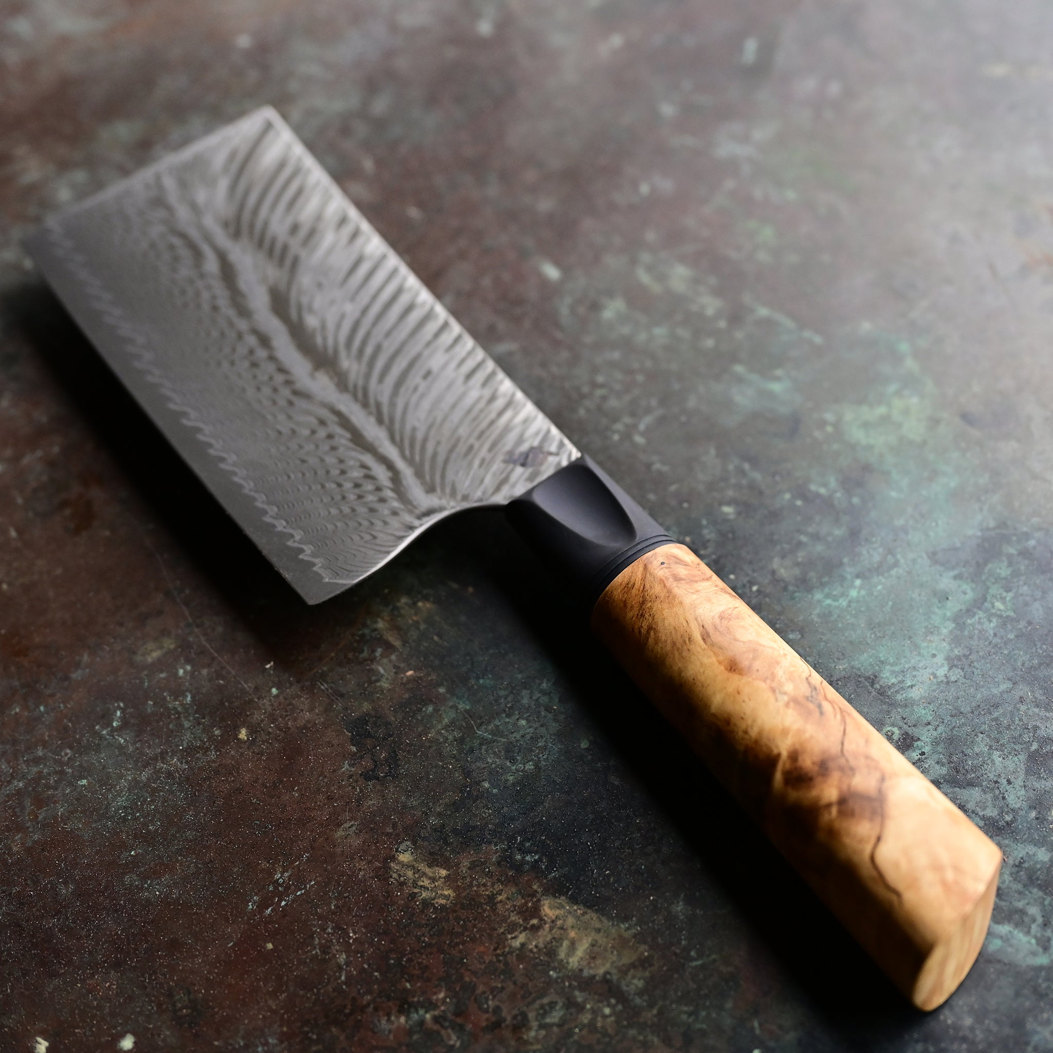 Unique mini cleaver on a concrete background, featuring a 4.5" long feather Damascus VG10 stainless blade, a sleek black anodized bolster, and a stabilized golden Buckeye burl wood handle with intricate patterns and color variations.